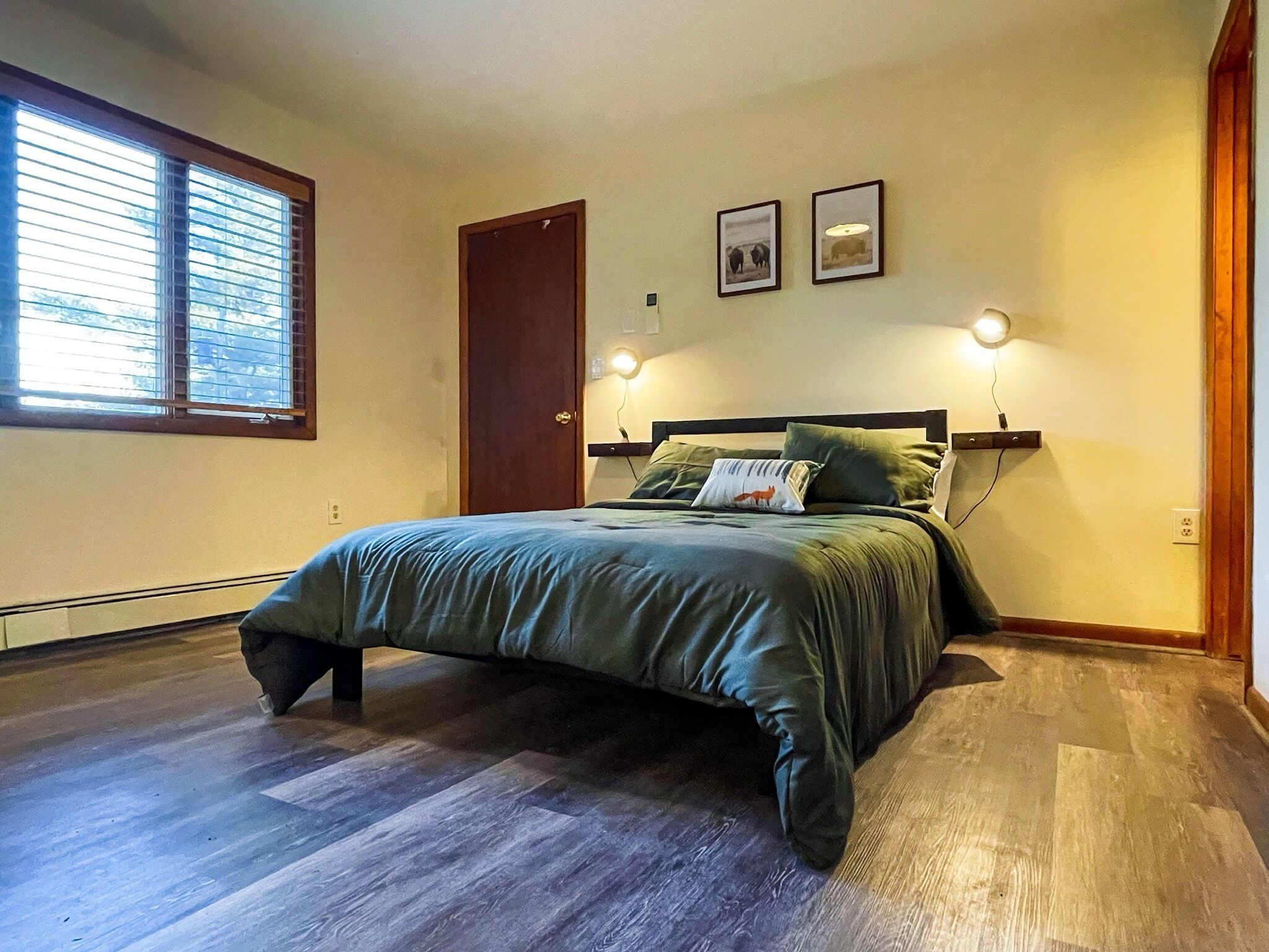 A bedroom with a bed, a window, a door, and two wall-mounted lights.