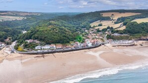 Vue aérienne d’une ville côtière avec une plage, une promenade et une colline couverte d’une végétation dense.