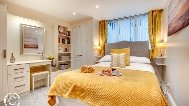 Une chambre d’hôtel comprenant un lit, des tables de chevet, une coiffeuse avec un miroir, une bibliothèque et une fenêtre avec des rideaux.