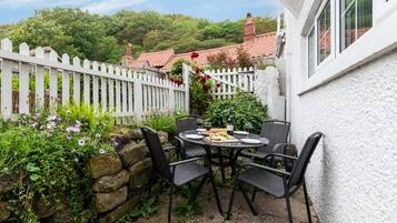 Eine Terrasse mit rundem Tisch und Stühlen, umgeben von einem weißen Zierzaun und üppigem Grün.
