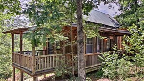 A wooden cabin with a deck, surrounded by trees and foliage. - Cabins at Brush Creek Mtn-Bear Den (Del Rio)