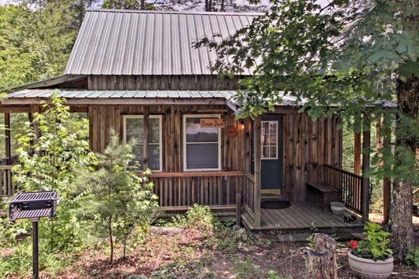 A rustic cabin with a porch, a front door, and a small window. - Cabins at Brush Creek Mtn-Bear Den (Del Rio)