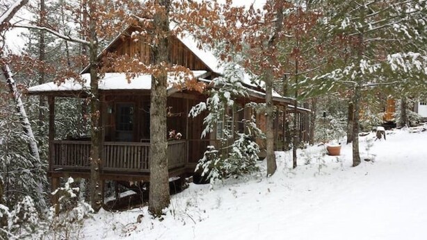A cabin with a wooden deck, surrounded by snow-covered trees. - Cabins at Brush Creek Mtn-Bear Den (Del Rio)