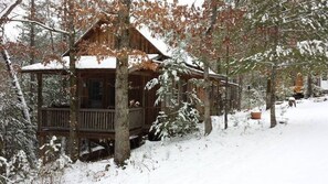 A cabin with a wooden deck, surrounded by snow-covered trees. - Cabins at Brush Creek Mtn-Bear Den (Del Rio)
