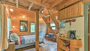 A cozy cabin interior with a wooden staircase, a bed with a view, a dining area, and a kitchen with basic amenities. - Cabins at Brush Creek Mtn-Bear Den (Del Rio)