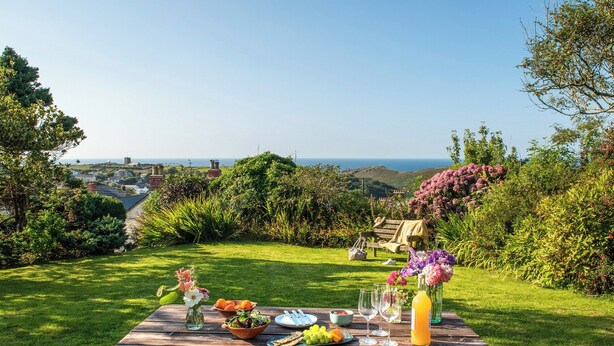 A picnic table set up on a grassy lawn with a scenic view of hills and a distant town. - 3 bedroom accommodation in Boscastle (Boscastle)