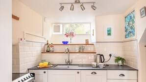 A kitchen with a stove, sink, and countertop. There are cabinets, a window, and a plant on the counter. - 3 bedroom accommodation in Boscastle (Boscastle)