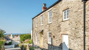 A stone building with a white door and windows, a narrow street, and a view of the sea. - 3 bedroom accommodation in Boscastle (Boscastle)
