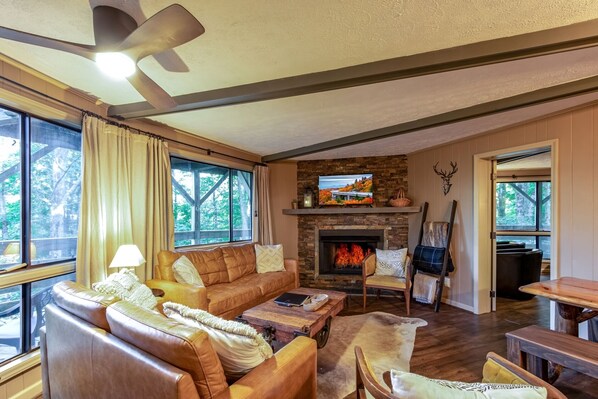 A cozy living room with a fireplace, leather sofas, a coffee table, and a television mounted above the fireplace.