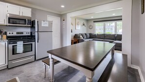 A modern kitchen with stainless steel appliances, a dining table, and a grey sofa in the adjacent living area. - Hamilton in heart of Omaha! Multi family and group friendly! The perfect space!! (Omaha)