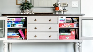 A white desk with drawers, a mirror above, and a shelf with board games. - Hamilton in heart of Omaha! Multi family and group friendly! The perfect space!! (Omaha)