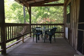 Eine Holzterrasse mit Tisch und Stühlen, umgeben von einem Hollerleger, mit Blick auf einen bewaldeten Bereich.