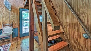 Uma escada de madeira em uma cabana, com vista para o exterior através de uma porta.