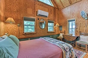 Ein gemütliches Cabin-Zimmer mit einem großen Bett, zwei Fenstern, einem runden Spiegel und einem kleinen Tisch mit einem Stuhl.