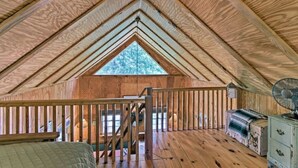 Quarto de sótão acolhedor com vigas de madeira, um clarabóia, escada de madeira e cômoda antiga.