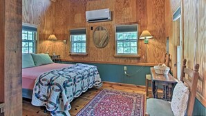 Quarto acolhedor de cabana com uma cama, duas janelas, um ventilador e uma pequena mesa.