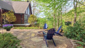Uma cabana de toras com um alpendre de pedra, duas cadeiras Adirondack e um braseiro.