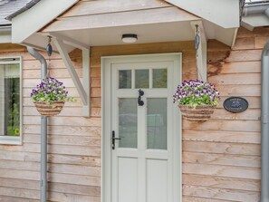 Un chalet en bois avec une porte blanche, deux jardinières suspendues et une enseigne indiquant « VIOLET COTTAGE ».