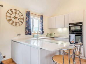 A modern kitchen with a central island, white cabinetry, a double oven, and a decorative clock. - 1 bedroom accommodation in Herford (Herford)