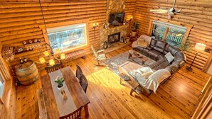 Accogliente interno di una baita in legno con camino in pietra, un divano in pelle, pavimento in legno e zona pranzo con tavolo e sedie.