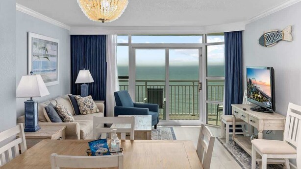 Une pièce comprenant un canapé, des fauteuils, une table à manger, un téléviseur et un balcon avec vue.