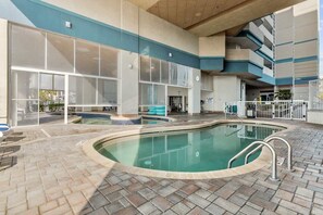 Una piscina interior con suelo de baldosas, una escalera de piscina y vistas al exterior del edificio.