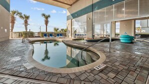 Un espace piscine doté d’un sol carrelé, de chaises longues et de palmiers en arrière-plan.