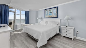 Une chambre à coucher avec un grand lit, une table de chevet, une commode, une fenêtre avec des rideaux et un tableau encadré au mur.