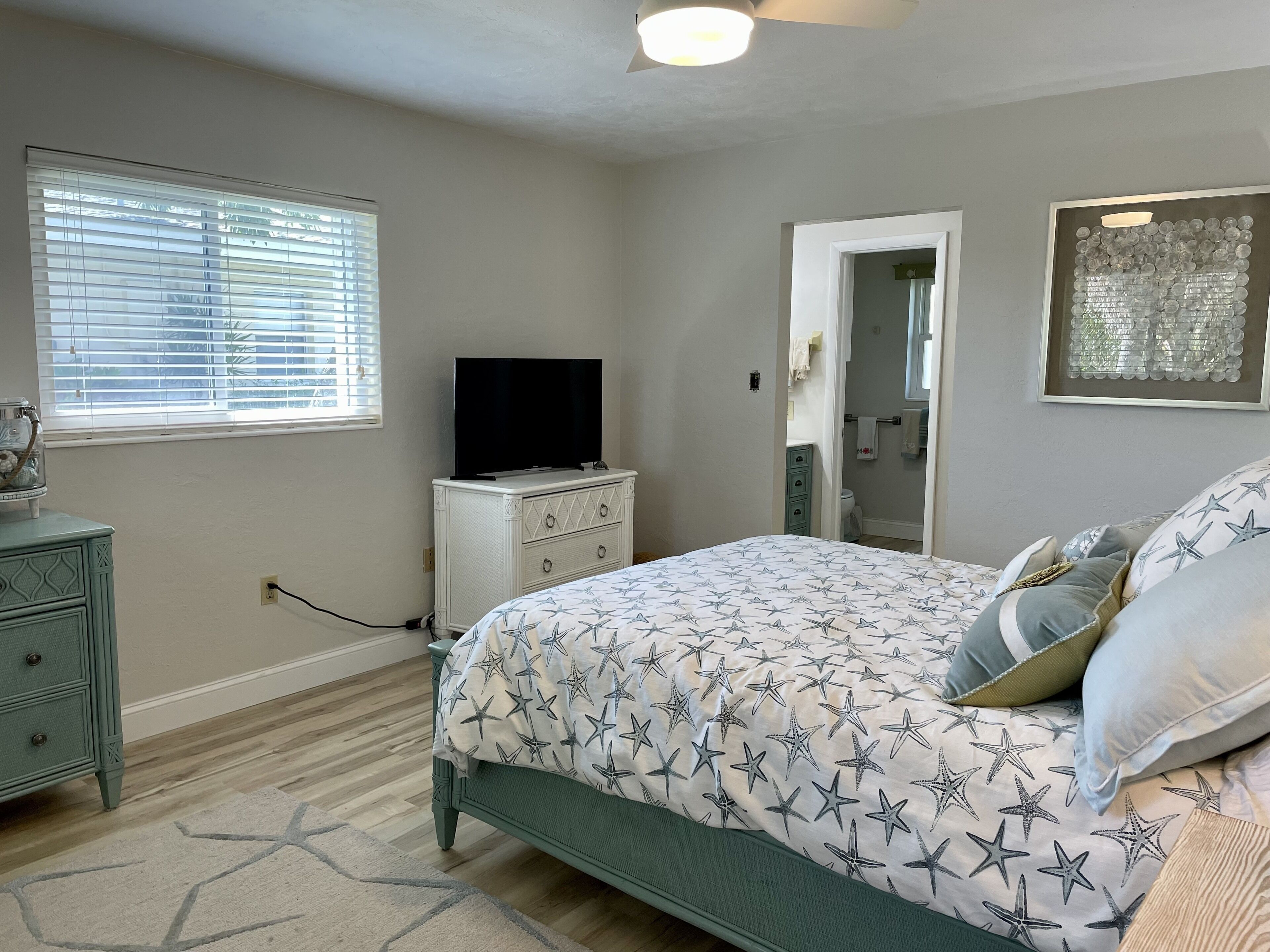 A bedroom with a bed, dresser, television, and a bathroom visible through an open door.