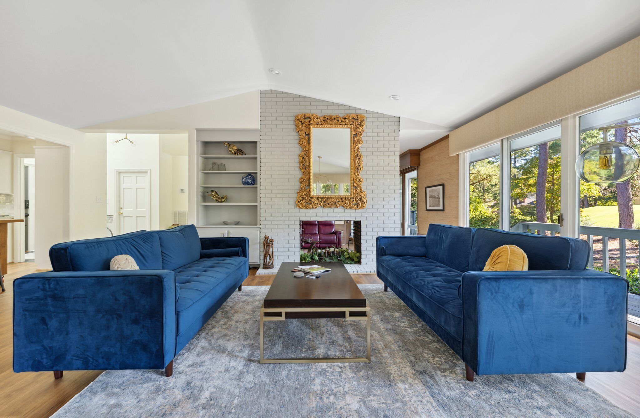 A modern living room with two blue sofas, a coffee table, and a fireplace with a decorative mirror above it.