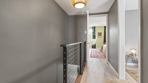 A hallway with a black metal railing, a woven light fixture, and a rug leading to a room with a bed. - Trendy Fishtown Mid-Century Modern Inspired Home (Philadelphia)