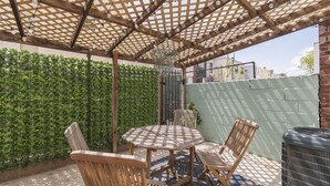 A covered patio area with a wooden table and chairs, a green wall, and a brick wall. - Trendy Fishtown Mid-Century Modern Inspired Home (Philadelphia)