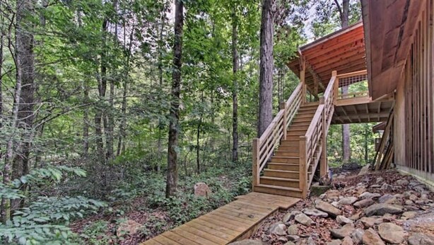 Uma cabana de madeira com uma escadaria que leva a um deck rodeado por uma floresta.