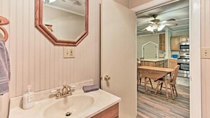 Casa de banho com lavatório, espelho e porta-toalhas. Uma porta dá acesso a uma sala de jantar com mesa e cadeiras.