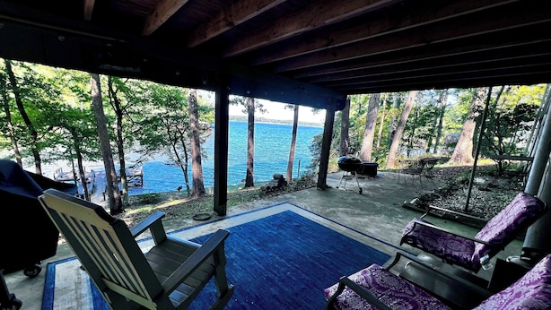 A covered outdoor seating area with a view of the sea, wooden chairs, and a barbecue grill. - Cozy Cabin with Screened Porch and Fishing Dock on Lake D'Arbonne (Downsville)