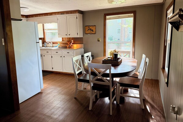 A kitchen with white cabinets, a dining table with chairs, and a window with a view of a house.