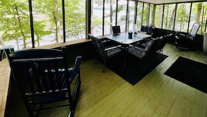 A room with a large window overlooking a lake, furnished with a table and chairs, and a wooden floor. - Cozy Cabin with Screened Porch and Fishing Dock on Lake D'Arbonne (Downsville)