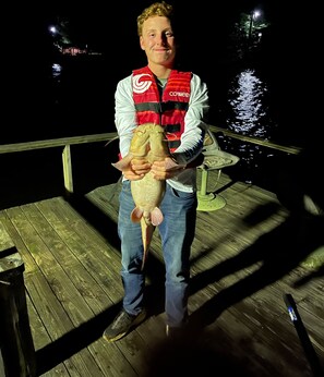 A person holding a fish on a wooden dock at night.