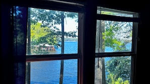A window with a view of a lake and trees, a lamp, and a small table. - Cozy Cabin with Screened Porch and Fishing Dock on Lake D'Arbonne (Downsville)