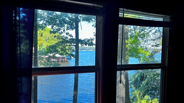 A window with a view of a lake and trees, a lamp, and a small table.