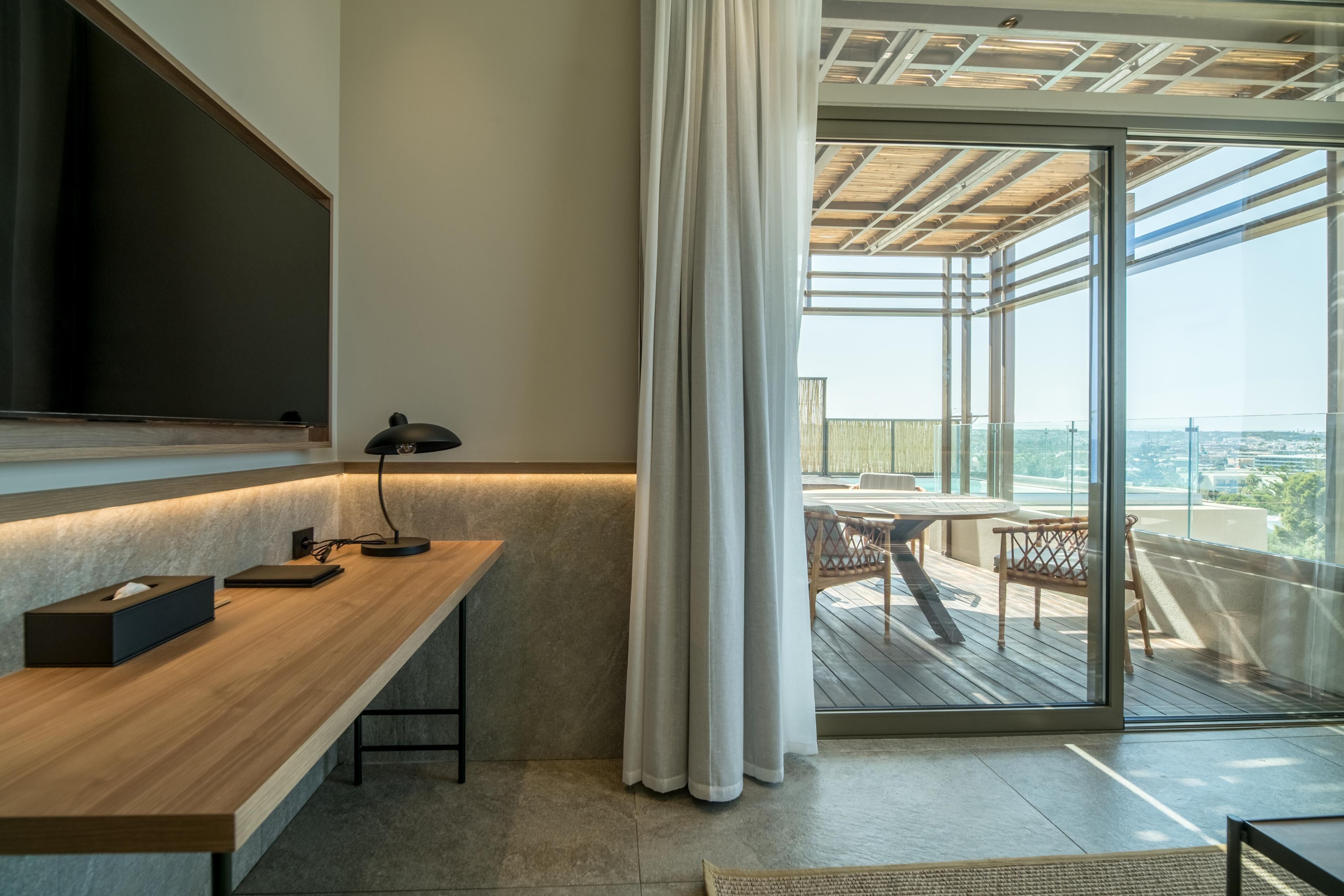 A modern room with a wooden desk, a black lamp, and a large window with a view of the city.
