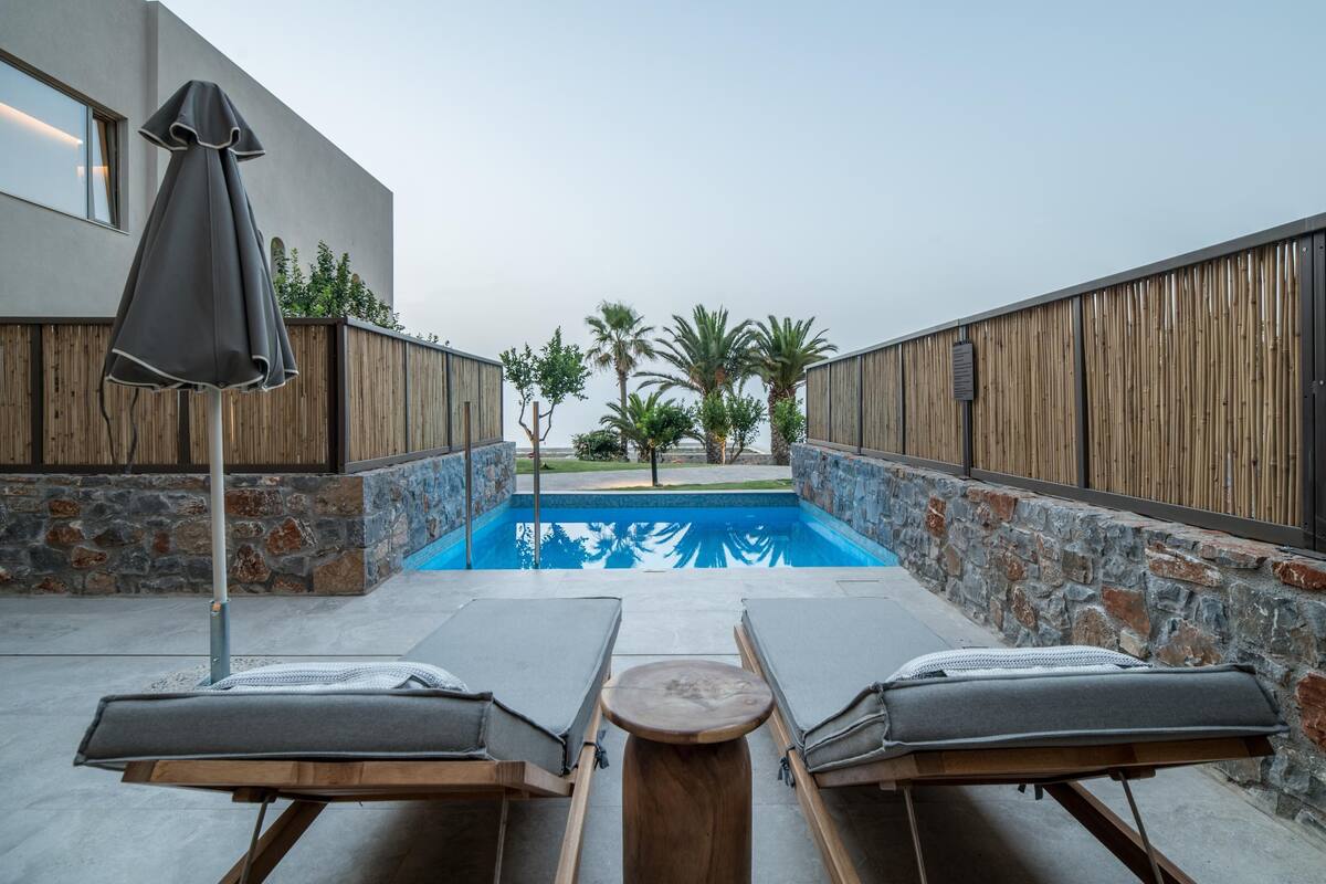 A pool area with lounge chairs and a table, surrounded by stone walls and wooden fencing.