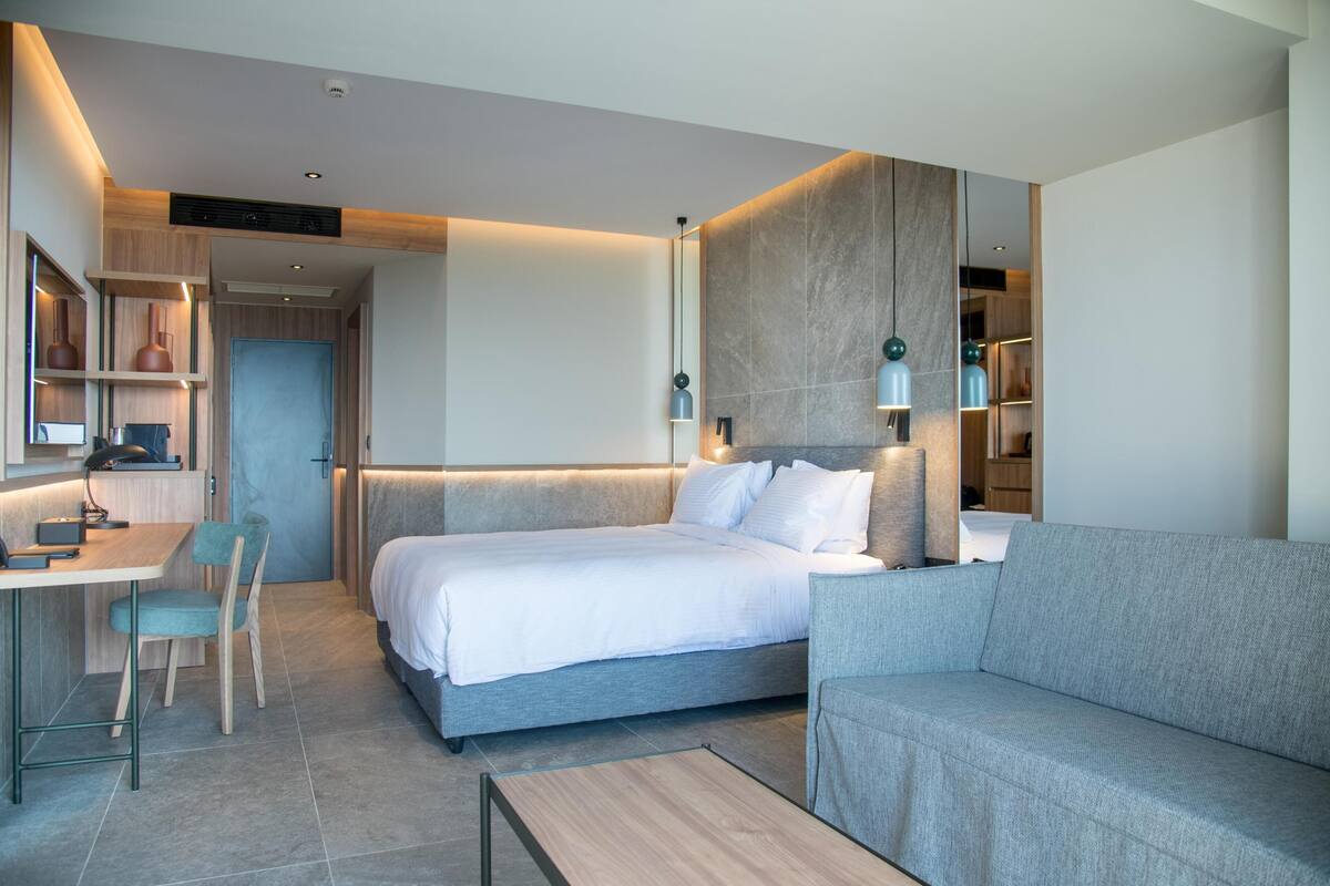 A modern hotel room with a bed, a sofa, a desk, and a chair.