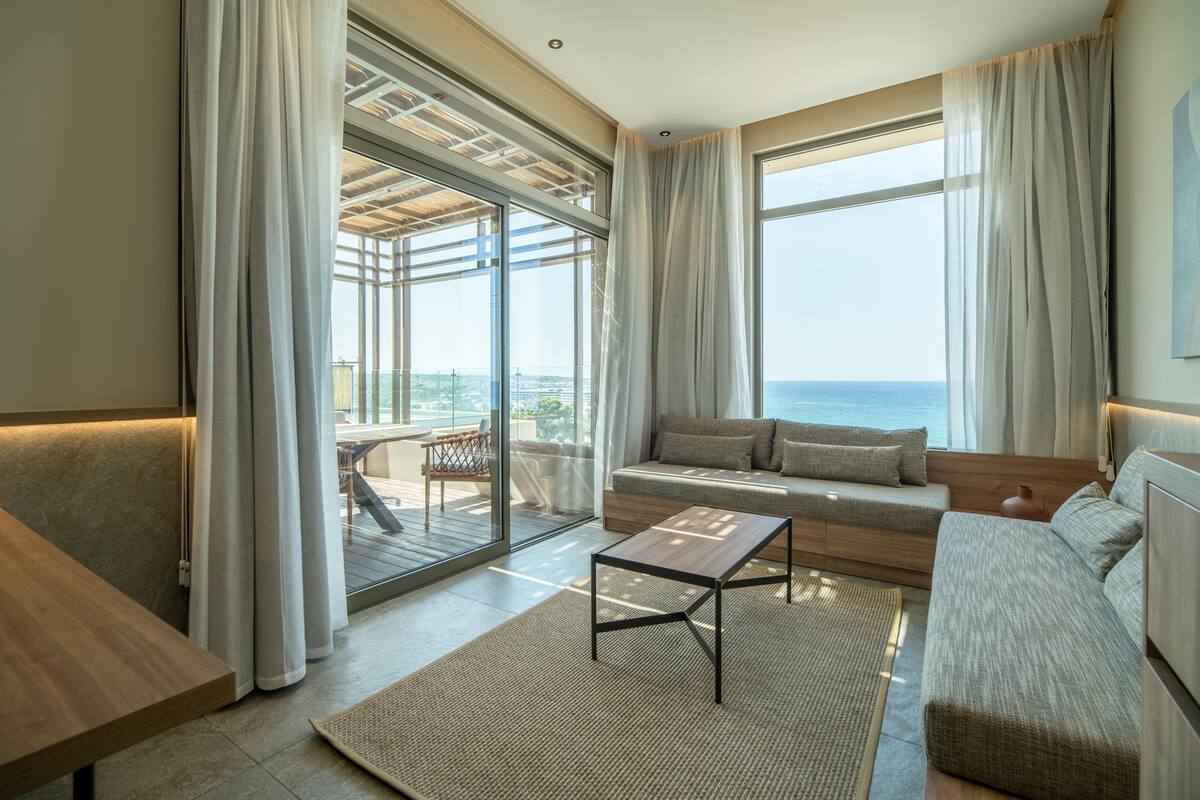 A modern living room with a sofa, a coffee table, and a view of the sea.