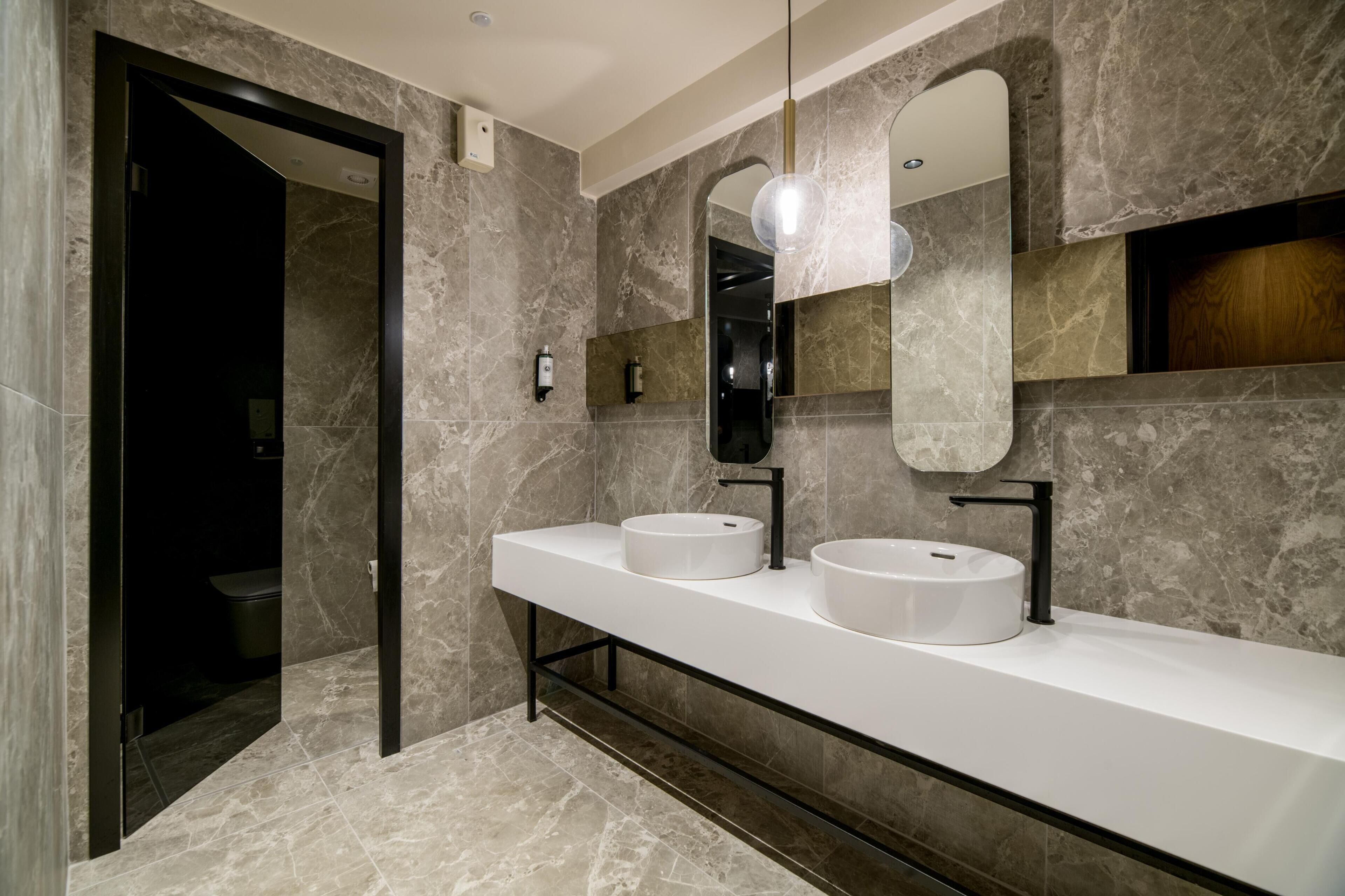 A modern bathroom with two sinks, a large mirror, and a walk-in shower.