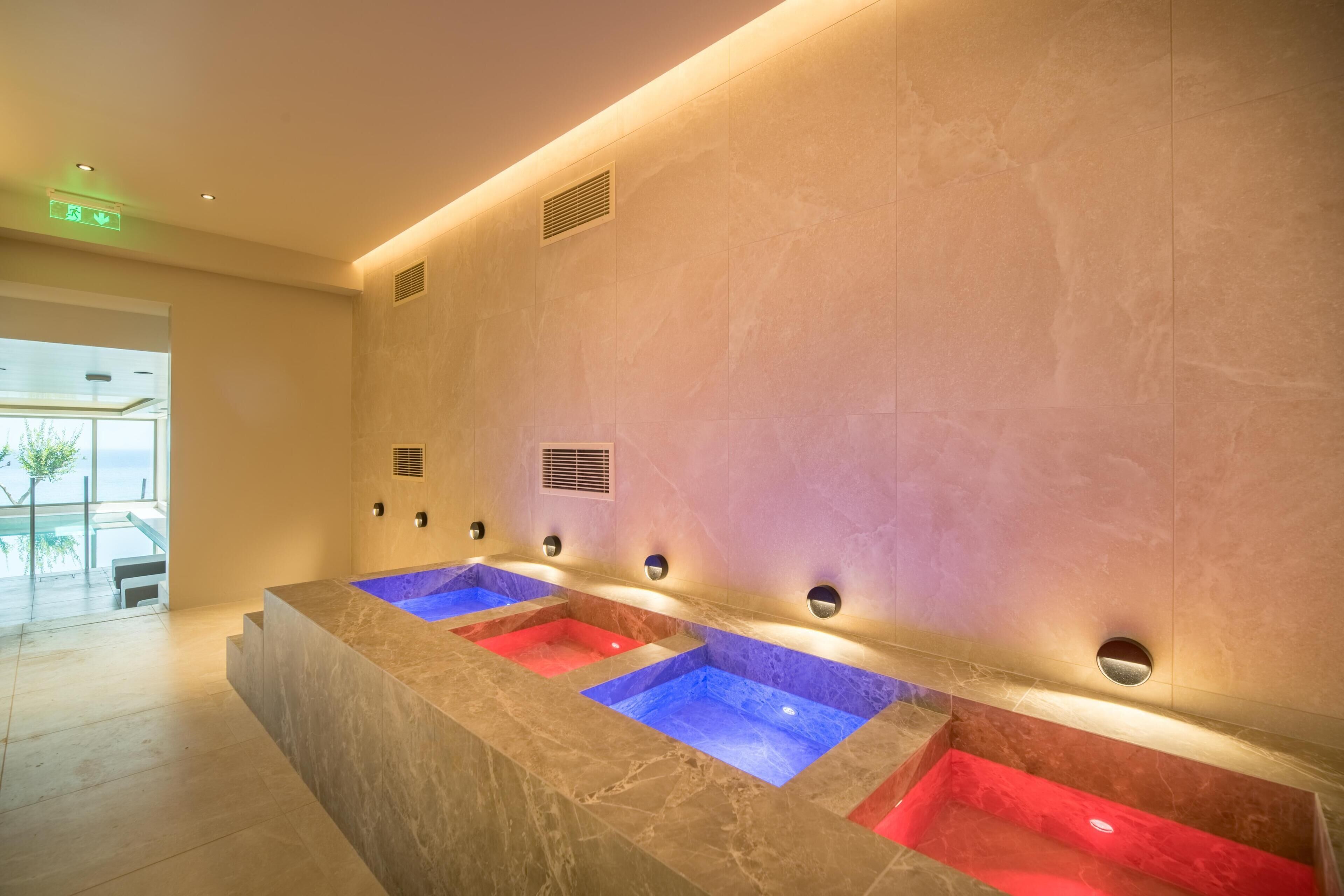 Un bagno moderno con diversi lavandini rossi e blu, un piano di lavoro in marmo e illuminazione a incasso.