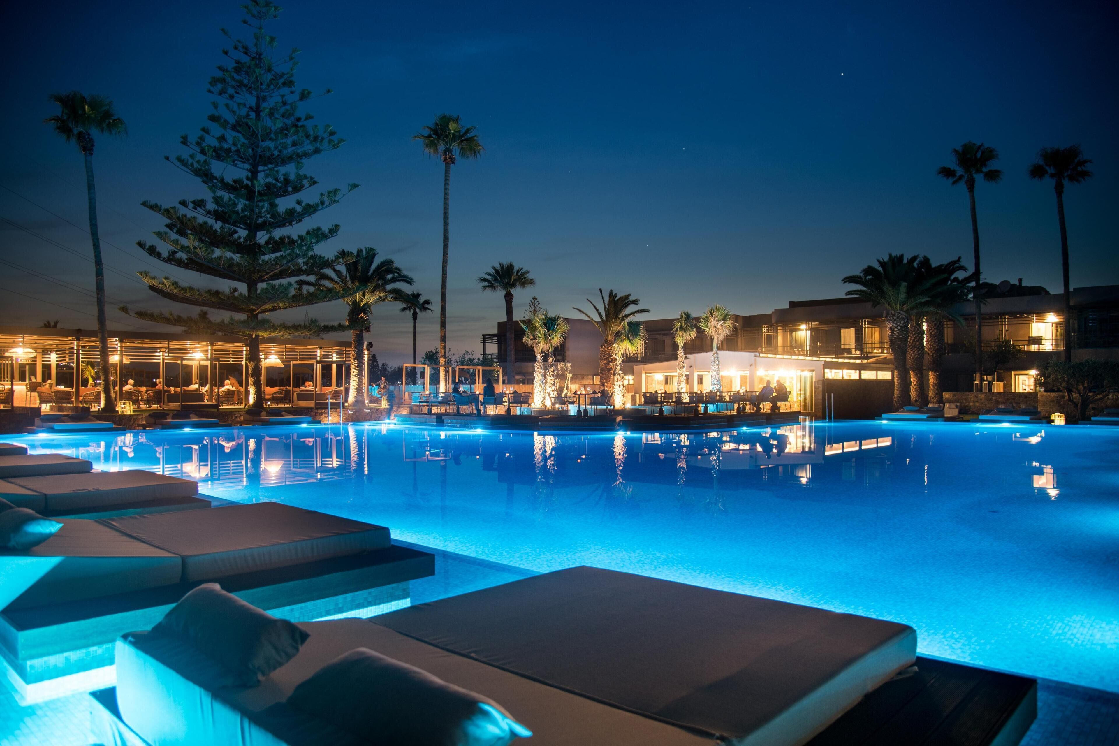 Zona de piscina nocturna amb gandules i palmeres.