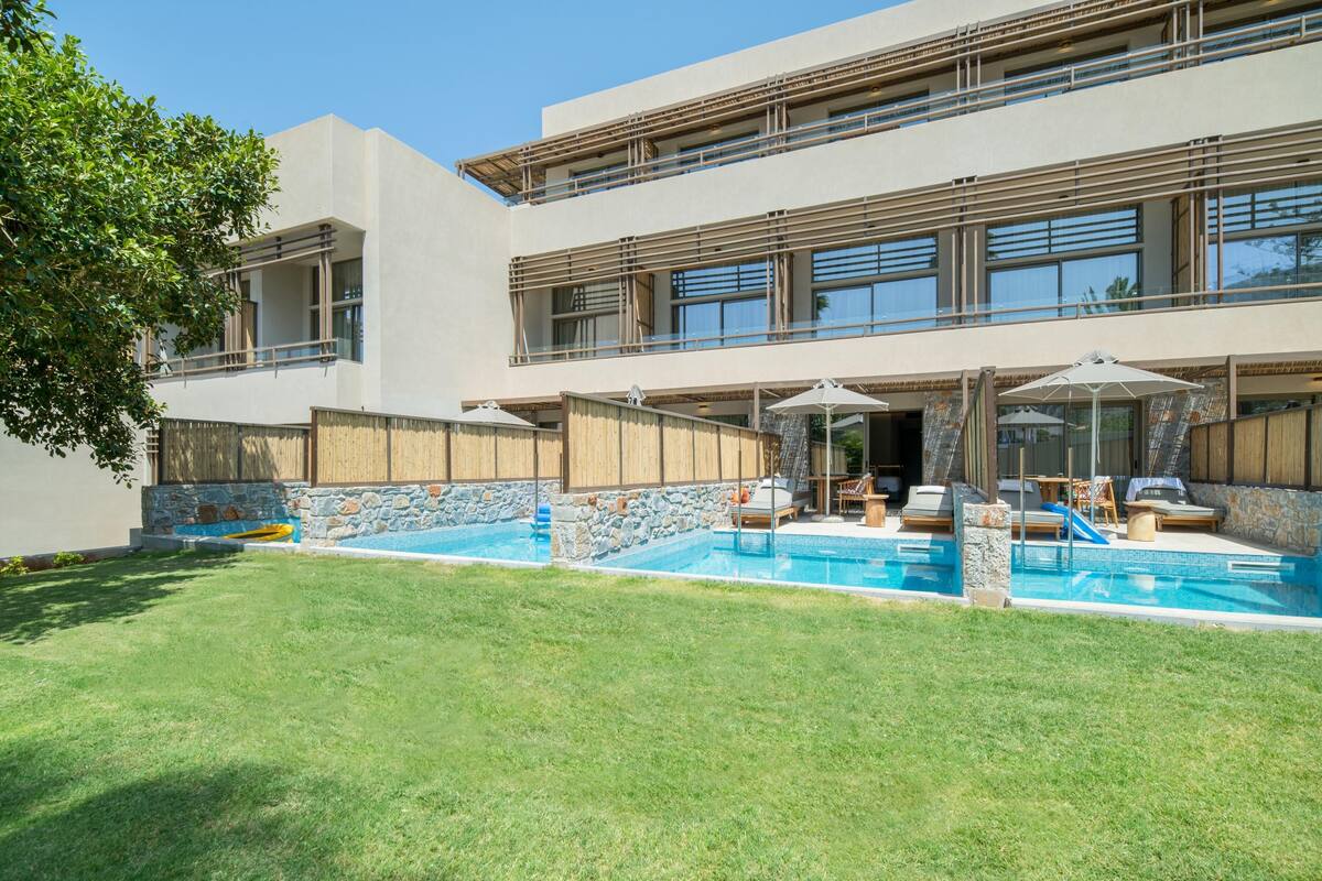 A modern building with a swimming pool, outdoor seating, and a stone wall.