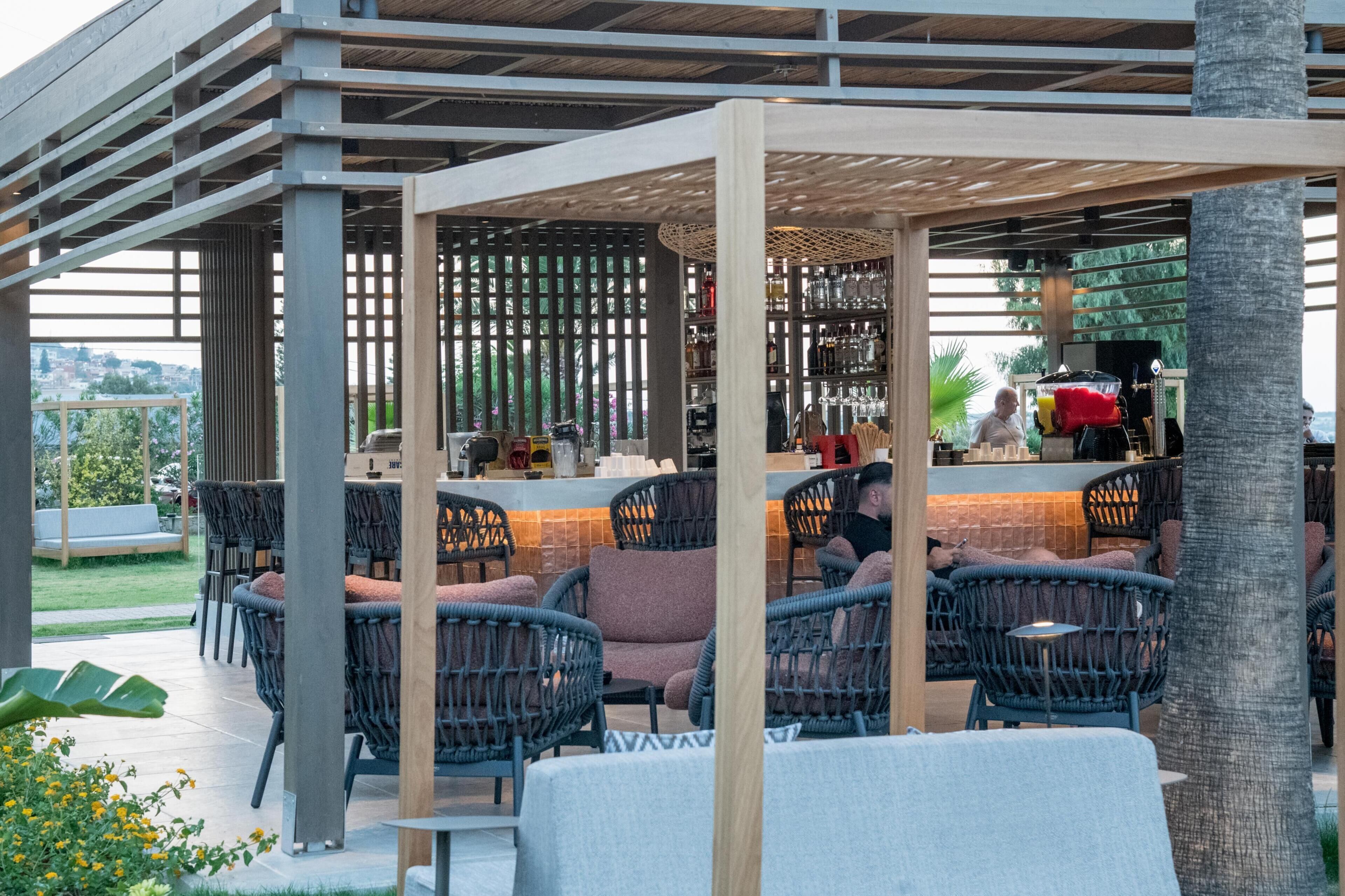 Un área de bar al aire libre con mobiliario de mimbre y una pérgola de madera.