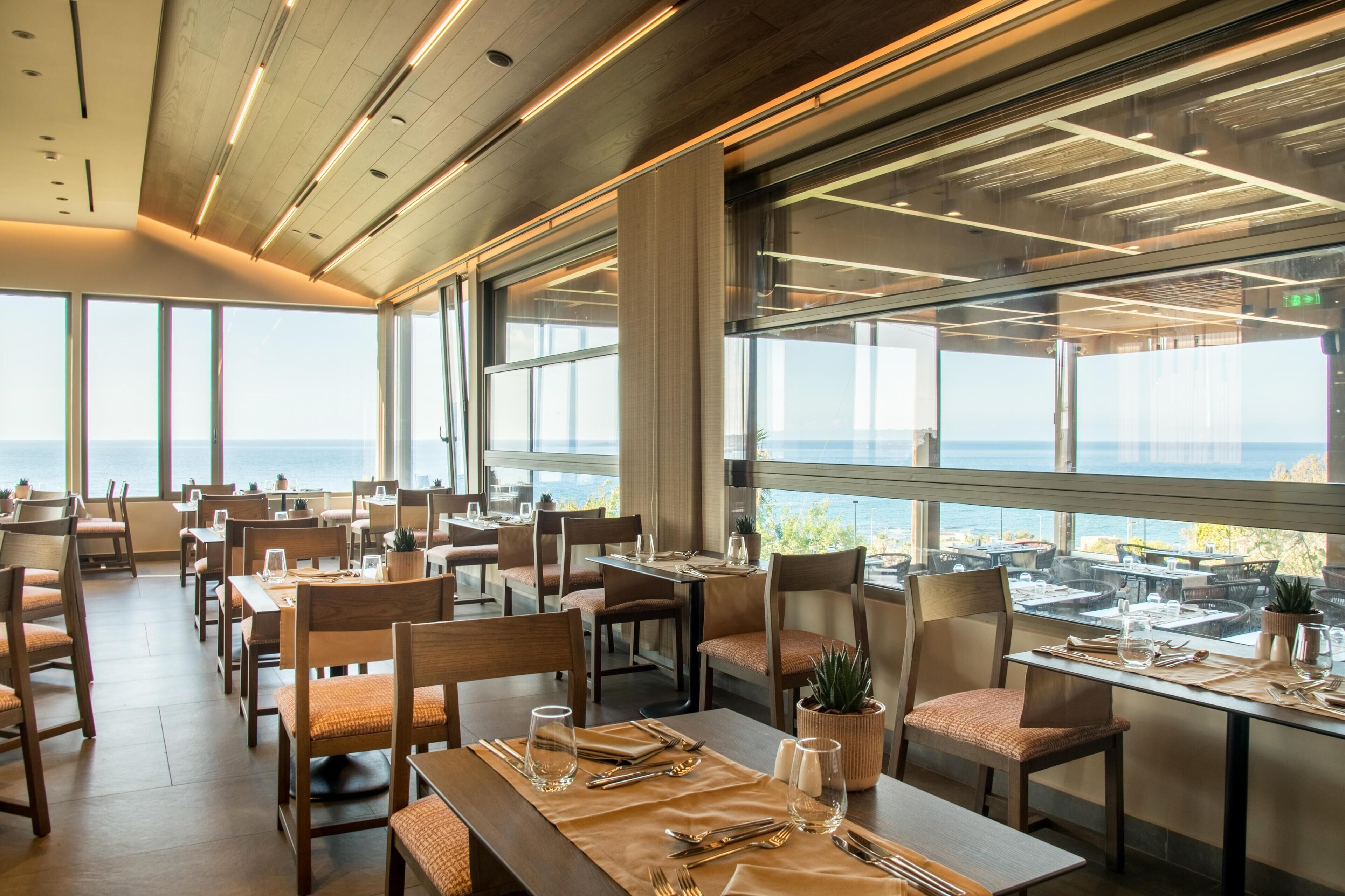 A restaurant with tables set for dining, large windows offering a view of the sea, and a modern interior design.